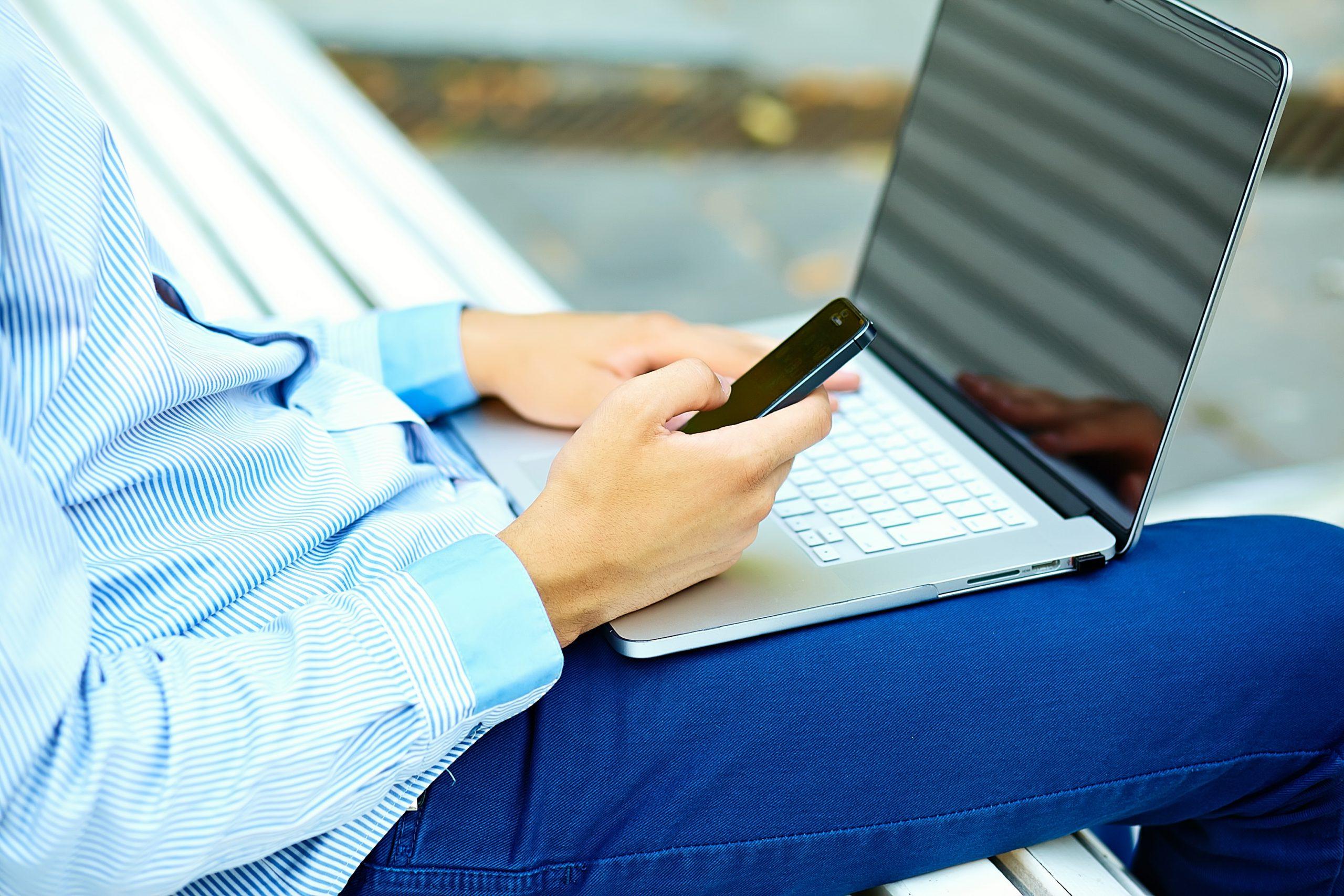 Young man working with laptop, man’s hands on notebook computer, business person in casual clothes in the street